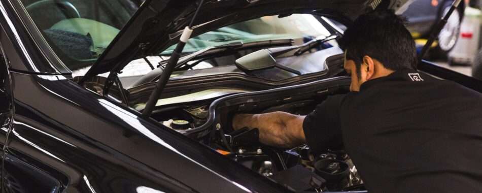 Mechanic working under the hood of a car, inspecting and repairing engine components.