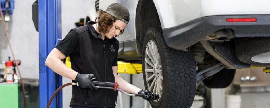 Mechanic inflating a tyre on a lifted vehicle in a workshop.
