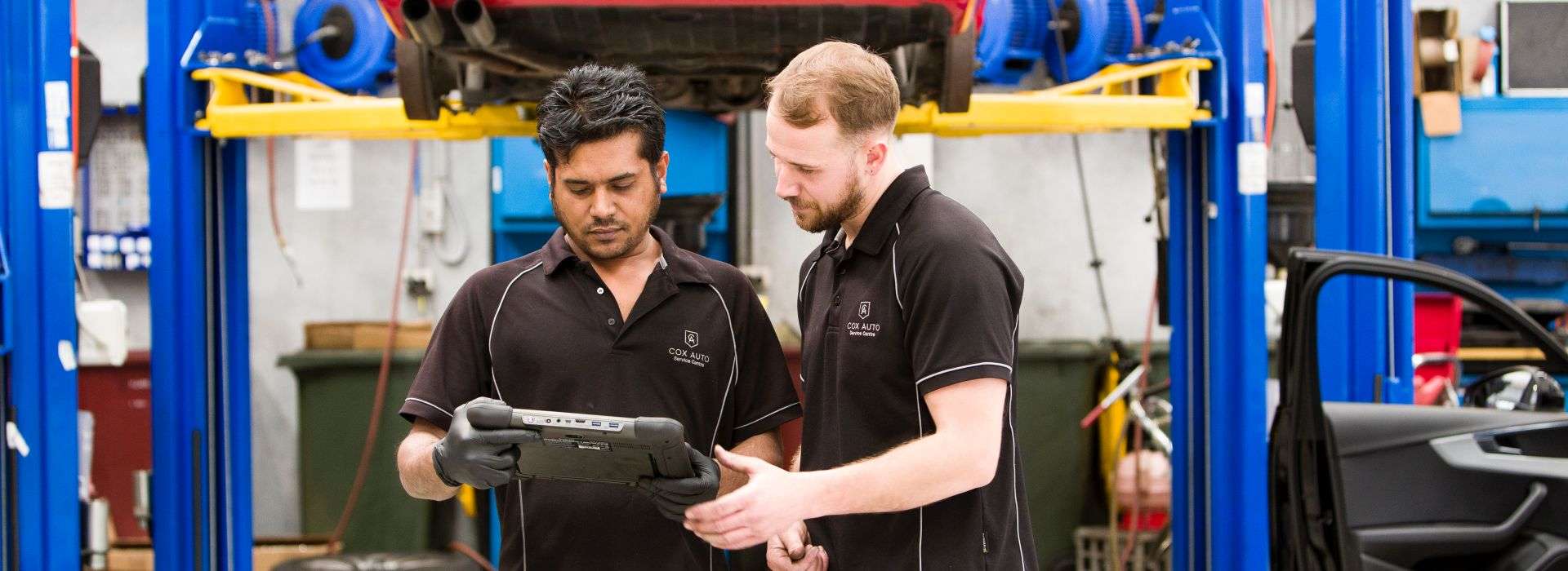 Two mechanics in a workshop reviewing information on a diagnostic tablet.