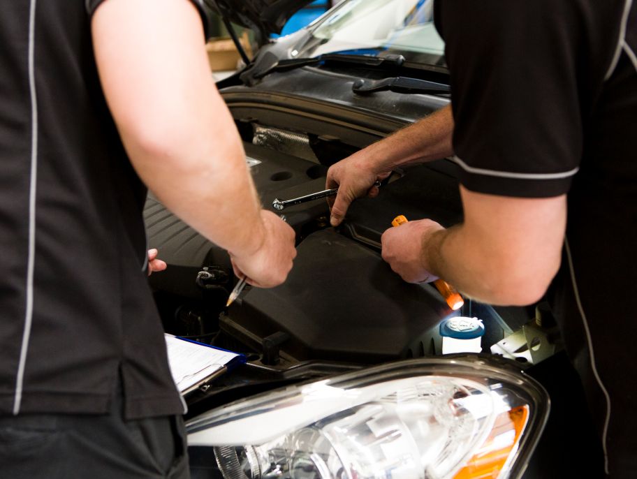 Two car service specialists looking over the engine of a vehicle.