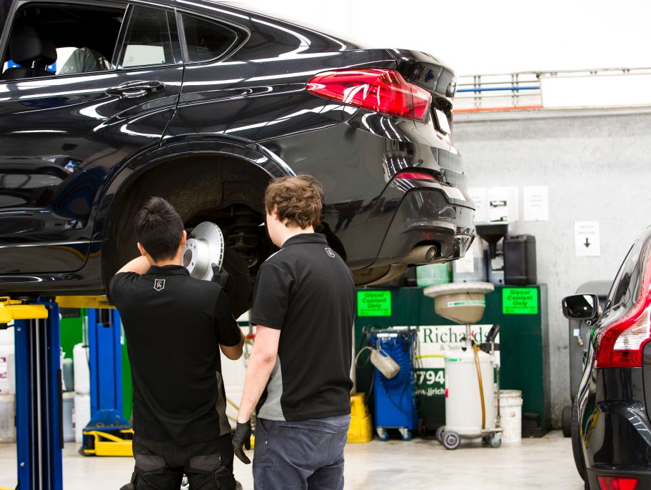Two Cox Auto mechanics inspect a car’s brake disks as part of a pre-purchase inspection.