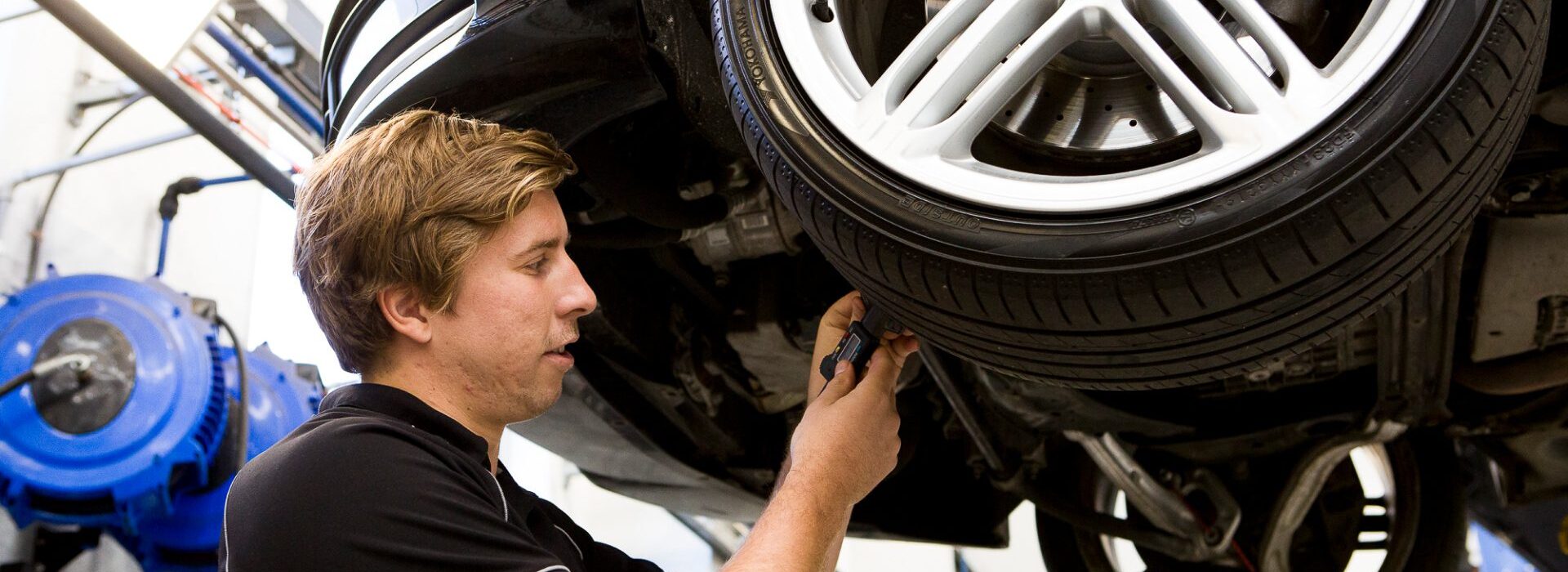 Mechanic inspecting the underside of a lifted Audi vehicle’s wheel area.