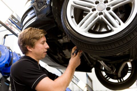 Mechanic inspecting the underside of a lifted Audi vehicle’s wheel area.