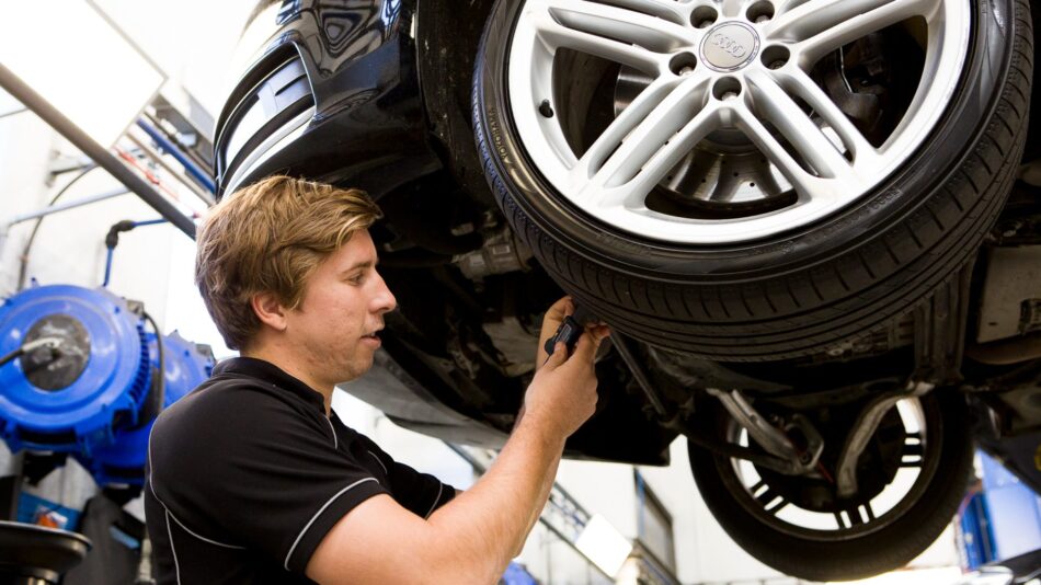 Mechanic inspecting the underside of a lifted Audi vehicle’s wheel area.