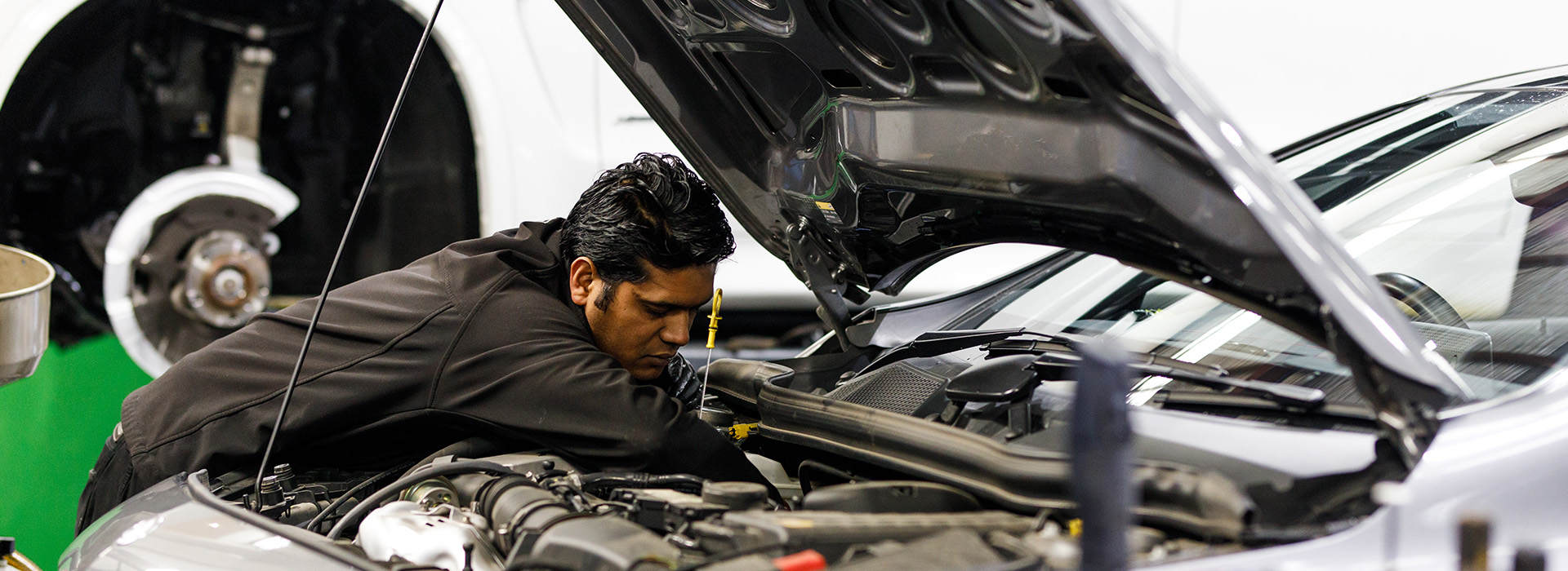 A car repair technician inspects the oil levels of a vehicle.