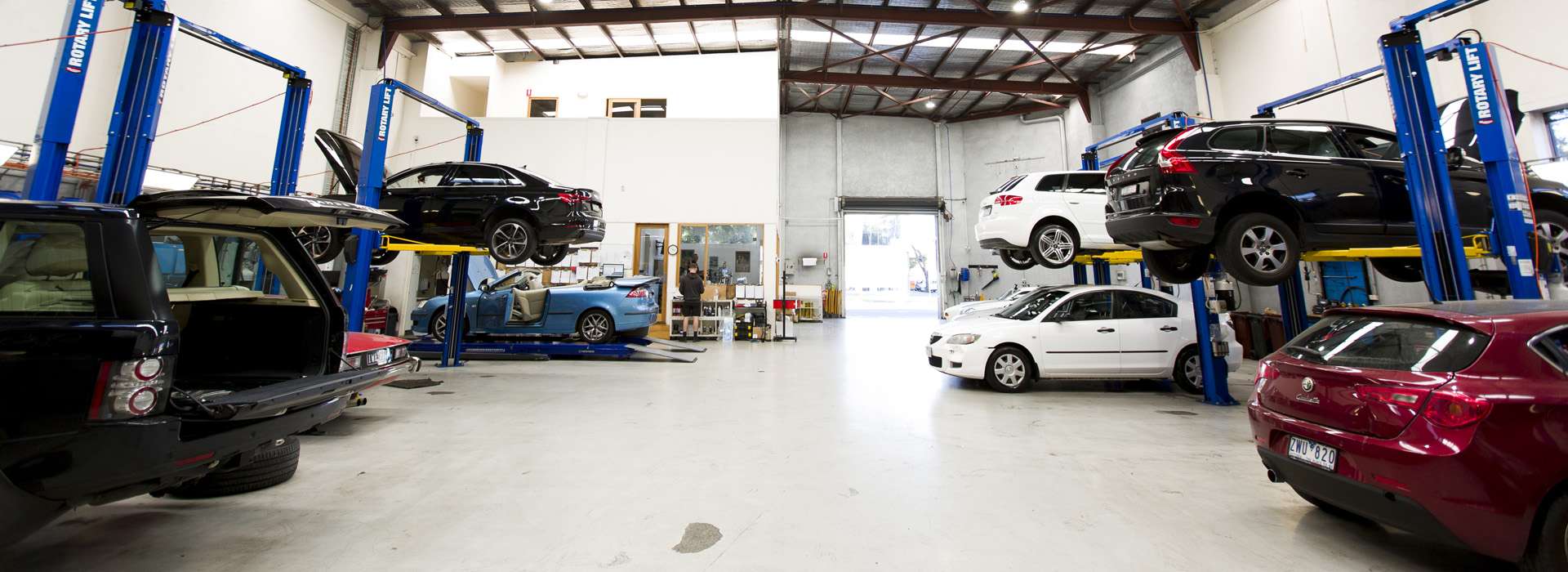 Interior of an automotive workshop with multiple vehicles on hydraulic lifts.