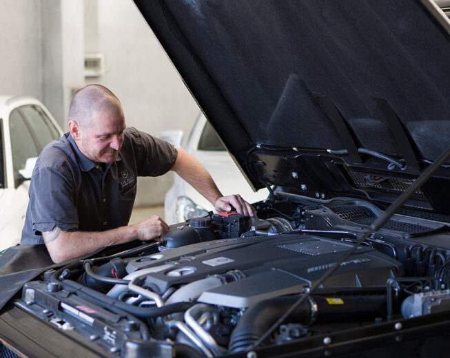 Mechanic inspecting the engine bay of a vehicle with the hood open.