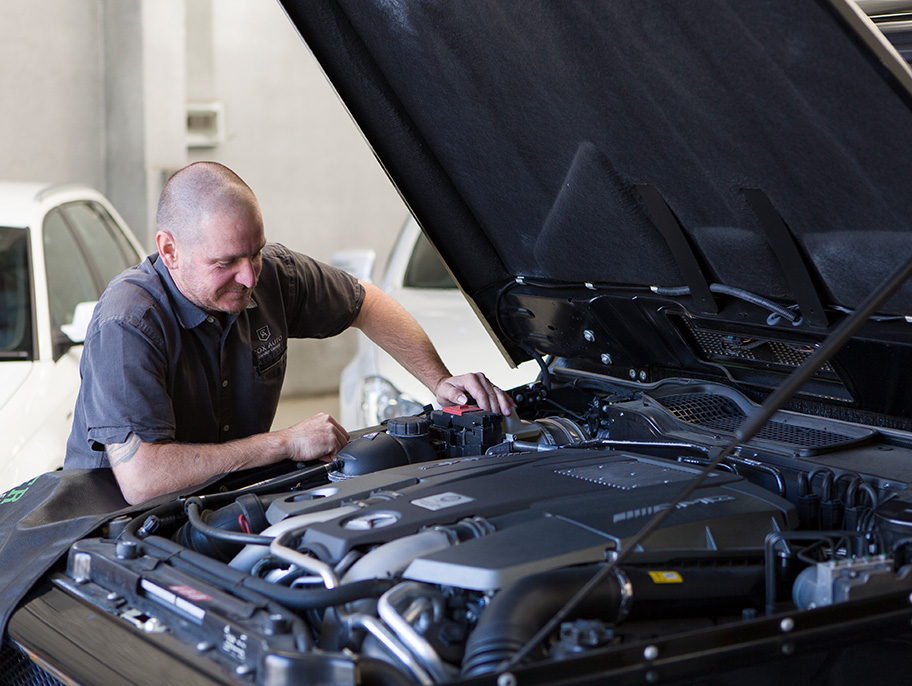Mechanic inspecting the engine bay of a vehicle with the hood open.