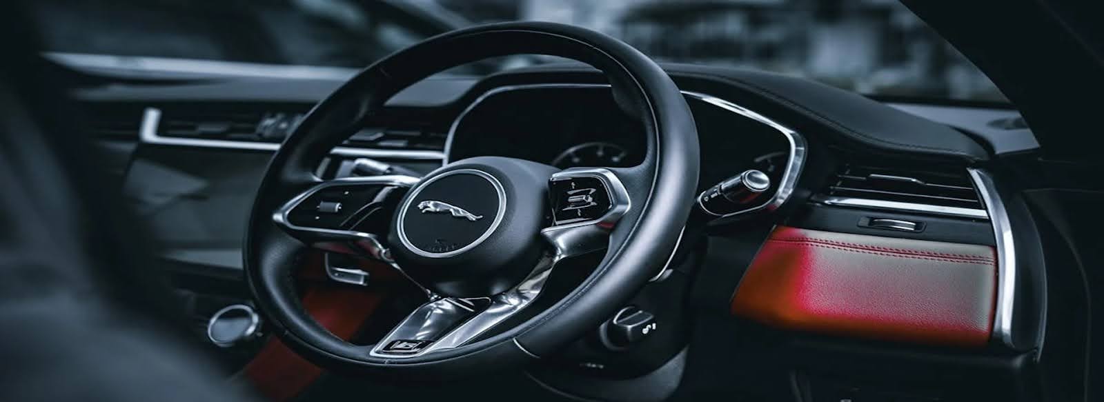 The Jaguar's steering wheel, wrapped in premium leather, offers a smooth, tactile feel, with brushed metal accents adding a touch of sophistication against the dark leather.
