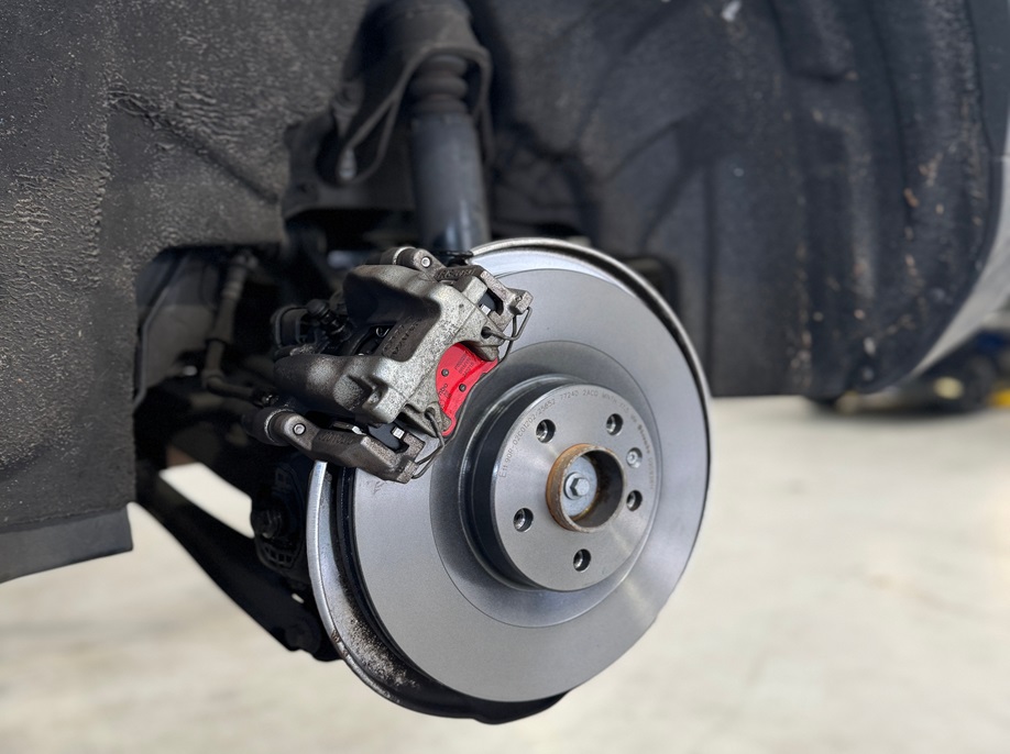 Close-up of a car’s brake disc and caliper with red brake pads.