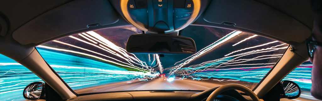 A vehicle navigates a tunnel, with colorful light trails from a long exposure shot creating a dynamic atmosphere around it.