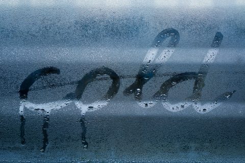 Someone has written the word 'cold' on a foggy car window.