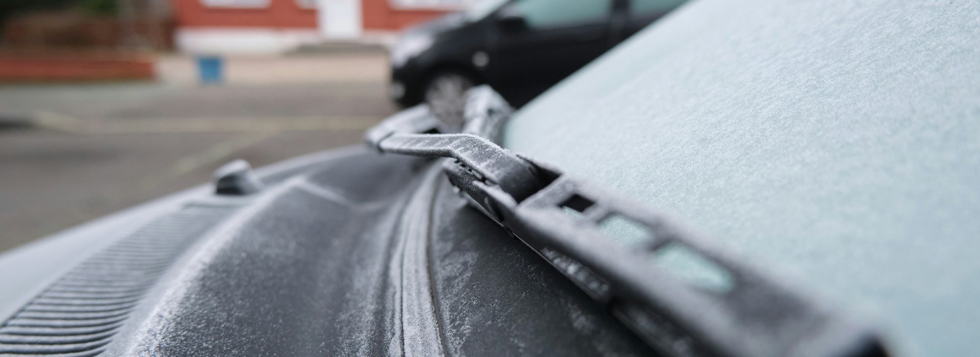 A dark coloured car is parked on a suburban street. There is frost on the windscreen.