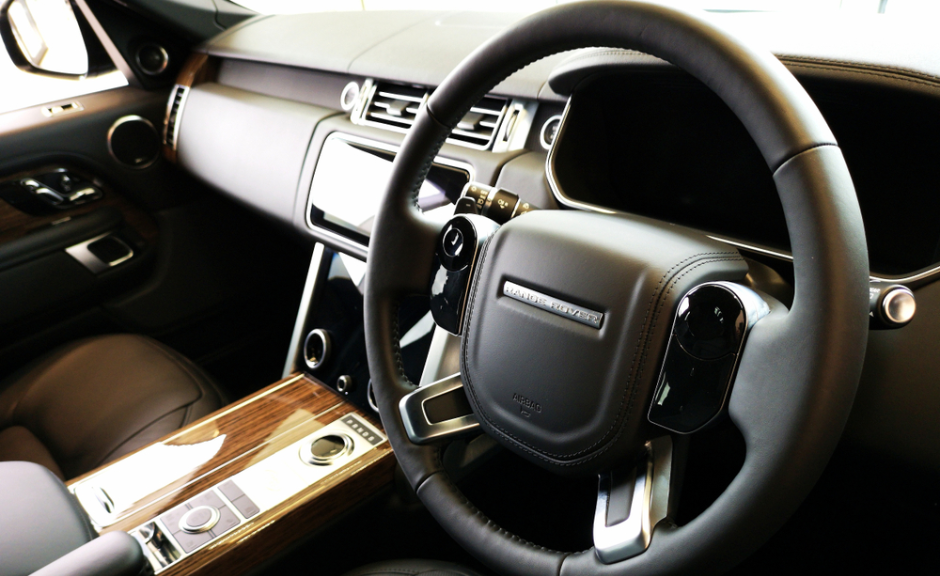 Close-up of a luxury Range Rover interior featuring leather steering wheel and woodgrain centre console.