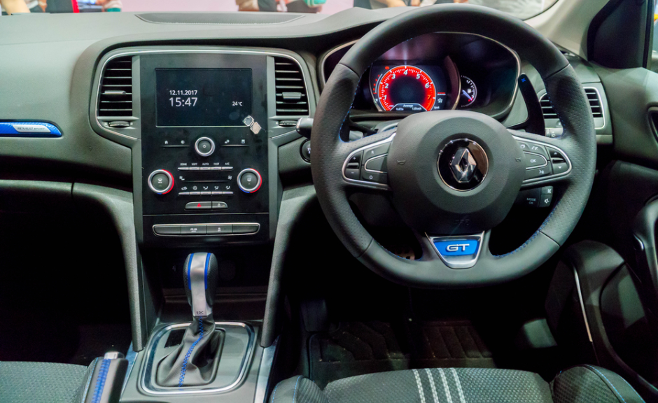 Interior view of a Renault GT showing the dashboard, touchscreen, steering wheel, and gear selector with sporty blue accents.