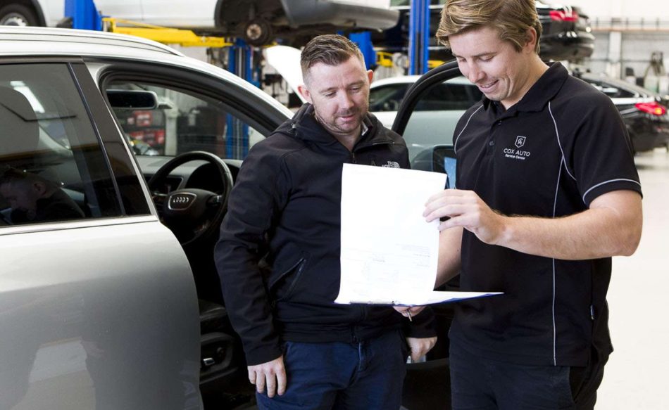 Two Cox Auto mechanics reviewing their pre-purchase inspection checklist before writing up a detailed report for their client.