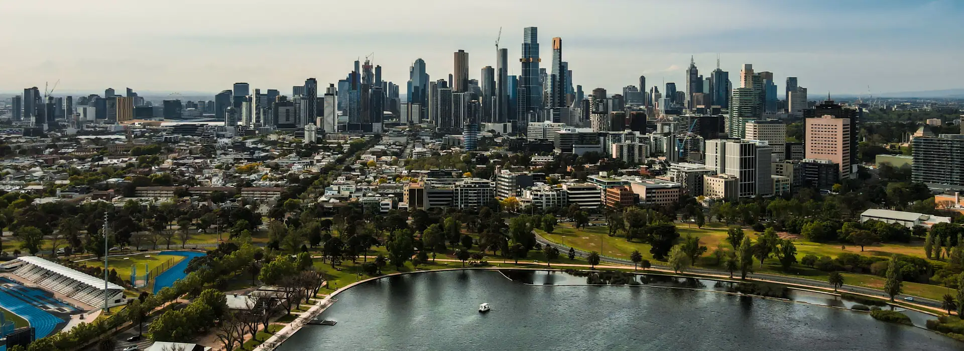 Urban skyline of Melbourne with modern skyscrapers and lush parkland along the Yarra River, highlighting the vibrant city atmosphere and scenic waterfront.
