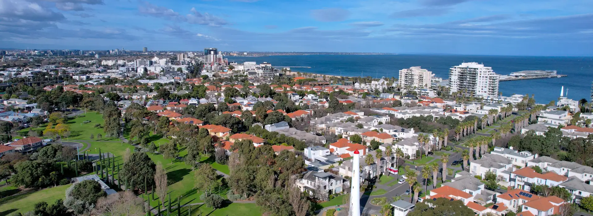 Vibrant aerial view of a coastal residential neighbourhood with modern homes, lush greenery, and stunning ocean backdrop, highlighting real estate and lifestyle near the beach.