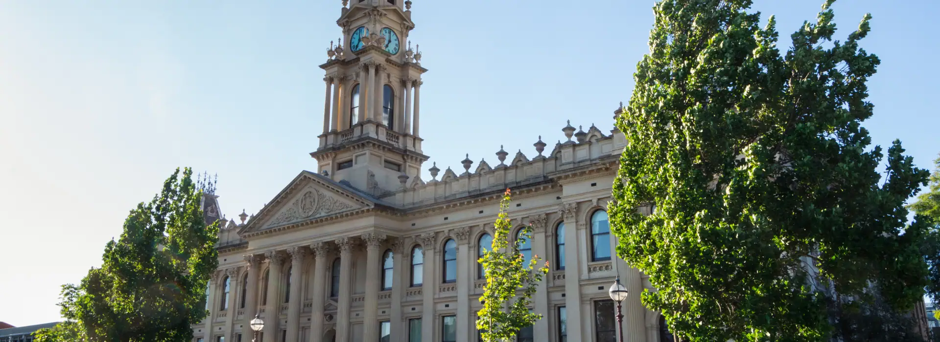 Historic city hall building with ornate architecture and tall clock tower surrounded by lush green trees in Brisbane, Queensland, Australia.