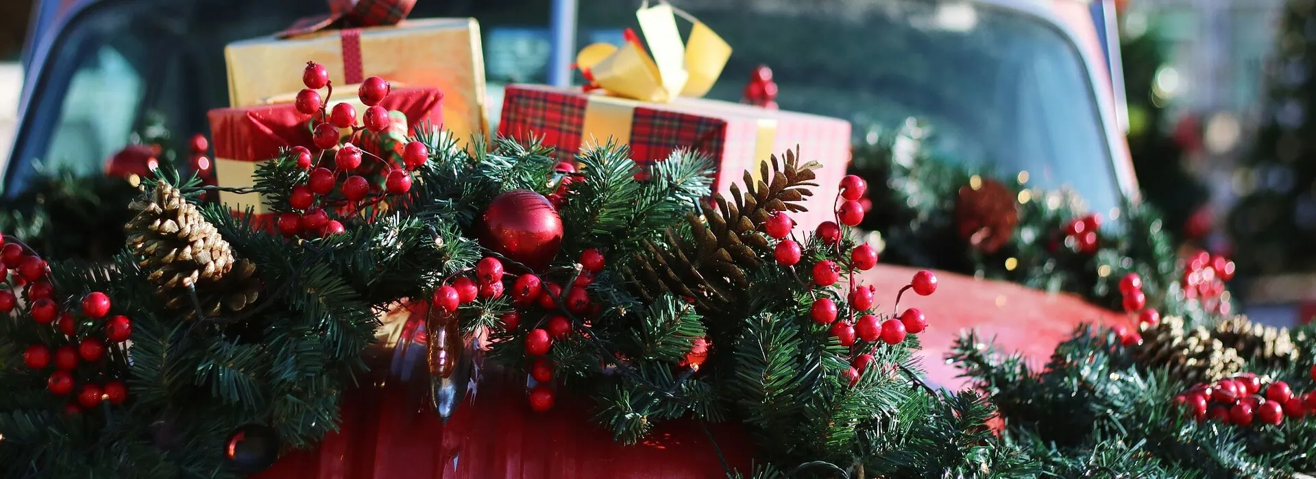 Festively decorated vintage car with Christmas wreaths and gifts for holiday celebration, featuring a Christmas tree in the background.