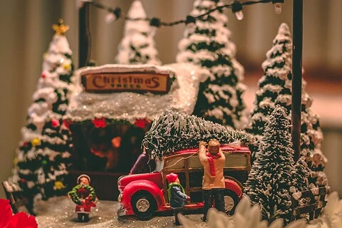 Miniature Christmas scene featuring a vintage red truck with a Santa figure loading a Christmas tree, surrounded by snow-dusted pine trees, holiday decorations, and a festive "Christmas" sign, perfect for holiday decor.