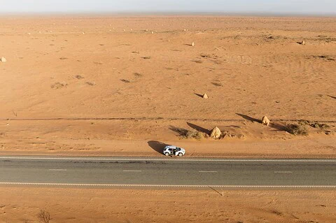 1. A white off-road vehicle parked on the side of a desert highway in a vast, arid landscape with sand dunes and scattered rocks, ideal for adventure and automotive protection.