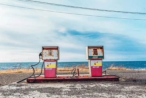 Fuel station pumps on a coastal road during daytime, with the ocean in the background.